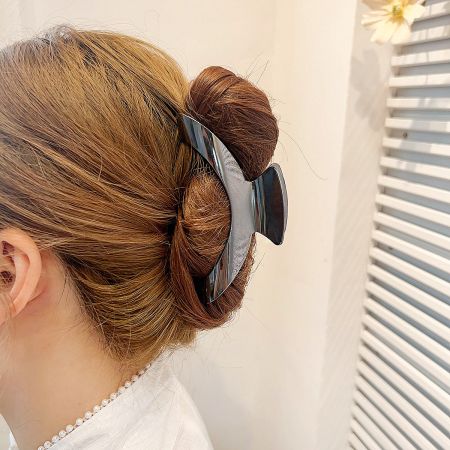 A woman with her hair styled in a bun, secured by a large black metal curve-shaped shark claw clip.