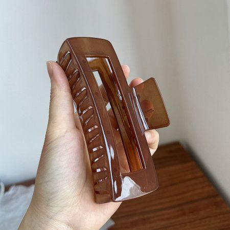 A large dark brown rectangle hair clip held in hand, highlighting its glossy finish.