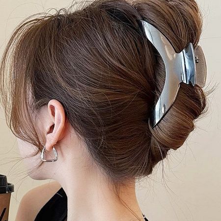 Close-up of a large silver metal curve-shaped shark claw clip holding a neat hair bun.