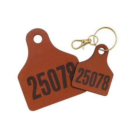 A close-up of a leather cow ear tag keychain next to a matching numbered tag, highlighting the authentic design.