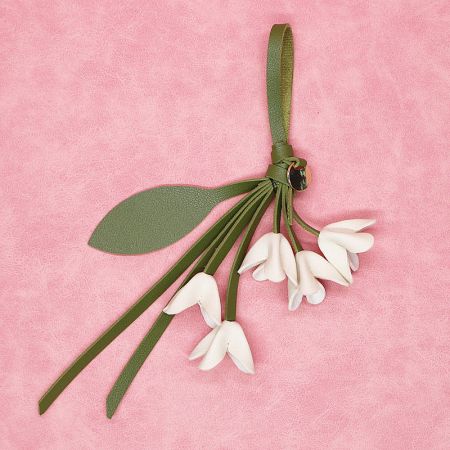 Close-up of a white PU leather flower bag charm with a green leaf strap against a pink background.