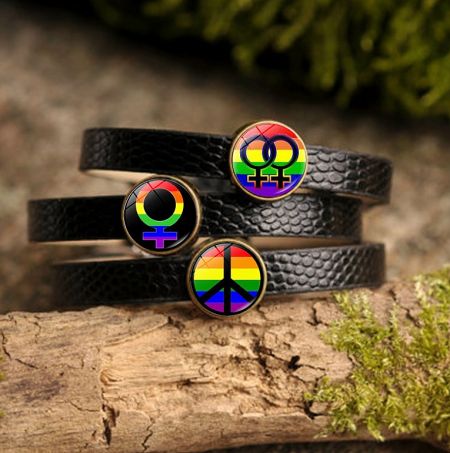 A collection of three black leather pride bracelets with different rainbow charms, including peace and love symbols.