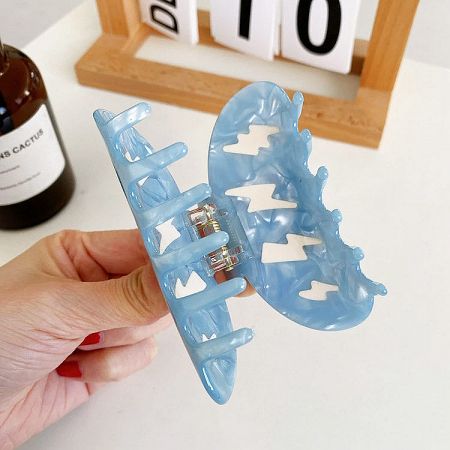 A hand holding a light blue claw hair clip, showing its unique design and spring mechanism.