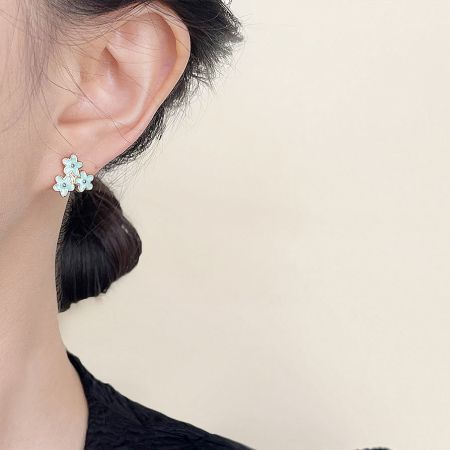 A pair of light blue flower-shaped earrings with gold centers being worn by a woman.