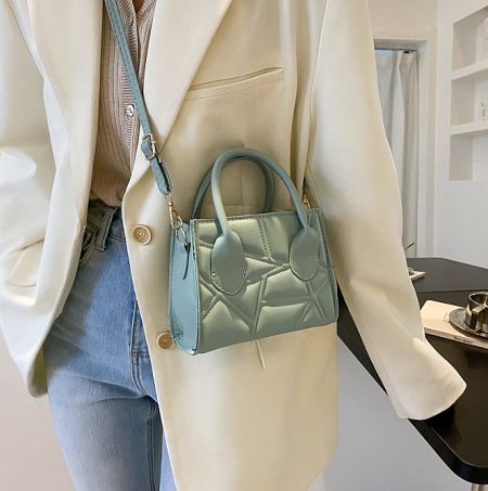 A close-up of a stylish light blue-green purse with a chic quilted design and gold chain strap.