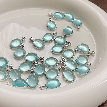 A collection of light blue, oval-shaped pendants with silver settings in a white bowl.