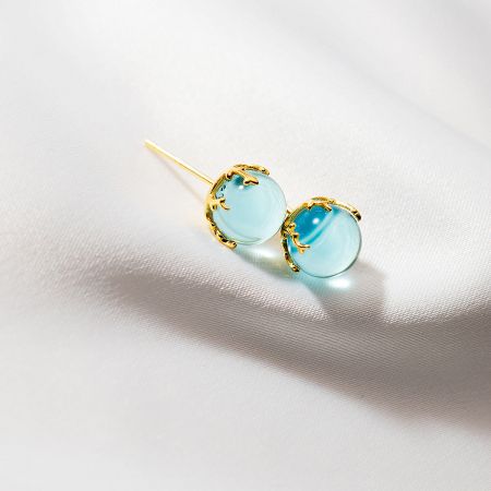 Close-up of the 925 silver mini blue crystal ball stud earrings with gold settings.
