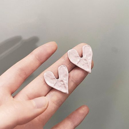 A close-up view of the pink enamel heart earrings held between fingers to highlight the hammered texture.