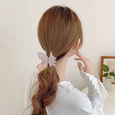 A woman wearing a light purple butterfly hair clip with her low ponytail.