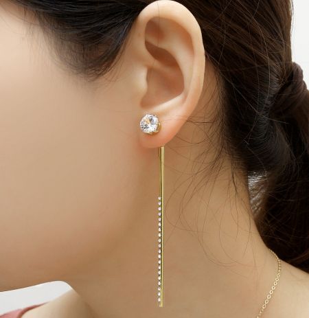 Close-up of the matching gold stud earring with a clear gemstone and dangling bar.