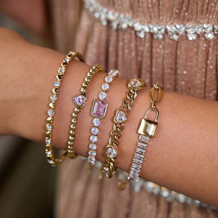 A stylish stack of gold and stainless steel bracelets, including the pink tennis bracelet, illustrating versatile styling options.