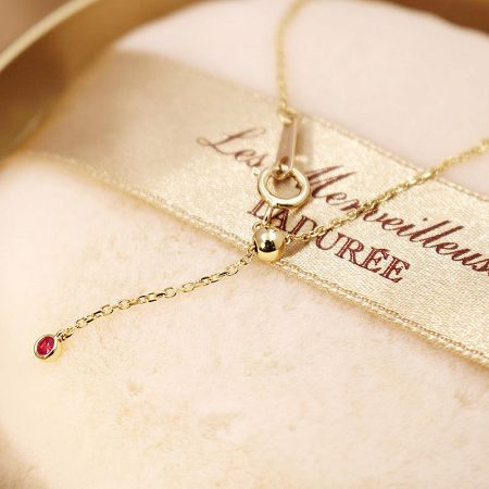 Close-up on a single red gemstone on the gold link chain, showing fine craftsmanship.
