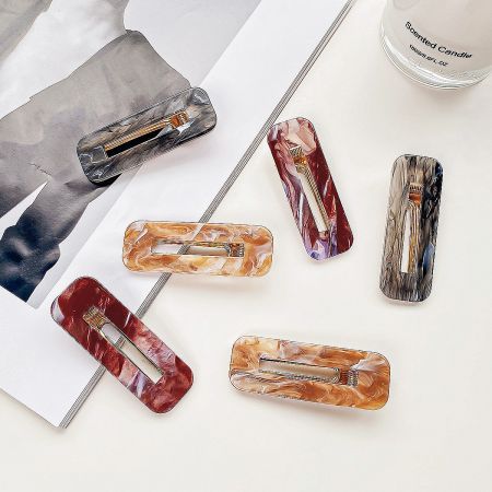 Lifestyle shot of colorful marbled hair clips arranged next to a lit scented candle.