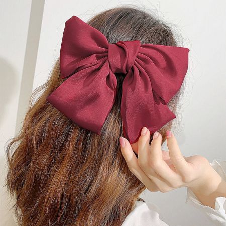 A woman wearing a large maroon fabric bow hair clip, showcasing its elegant style.