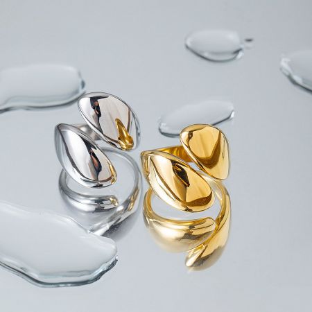 Two pairs of curved, polished stainless steel rings in silver and gold, with water droplets for a luxury feel.