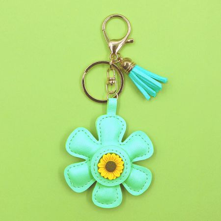 A mint green sunflower keychain with a turquoise tassel and gold clasp.