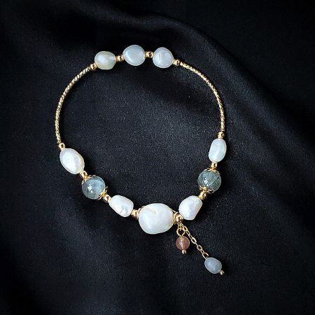 A beautiful moonstone and opal beaded bracelet with intricate gold details and a dangling charm.