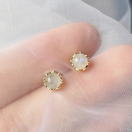 A gloved hand holding a pair of white shimmer stone earrings, highlighting their quality.