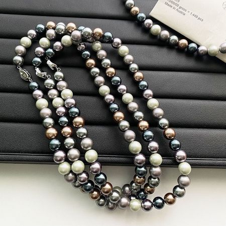 Multiple strands of Morandi-colored pearl necklaces arranged on a black display.