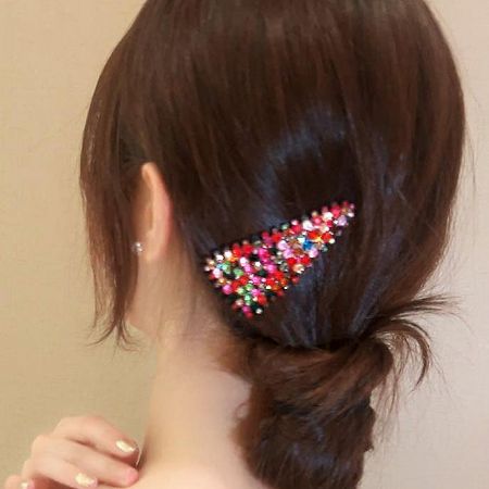 Close-up of a multicolored rhinestone hair clip securing a low bun hairstyle.