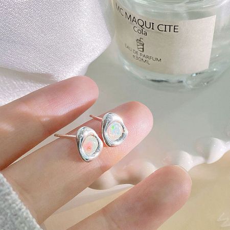 A pair of iridescent opal stud earrings displayed next to a stylish perfume bottle.