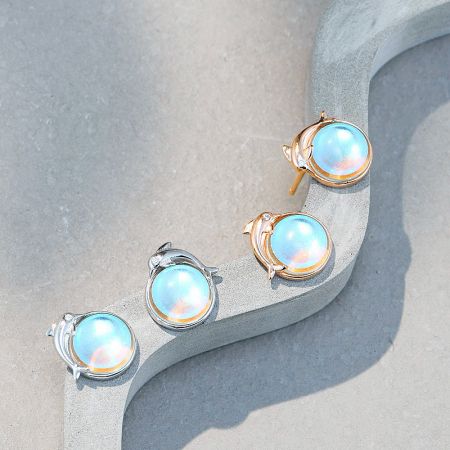 An assortment of silver and rose gold moonstone dolphin earrings displayed on a white surface.