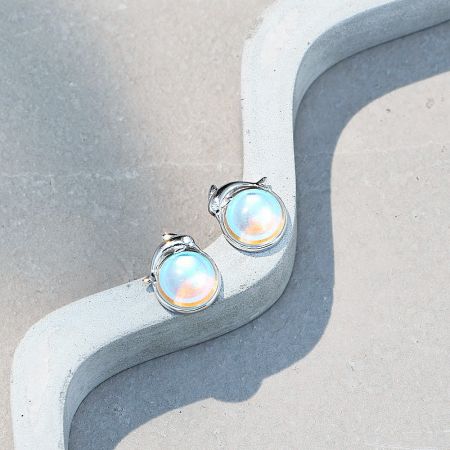 A detailed product shot of the moonstone dolphin stud earrings, highlighting the stone's color play.