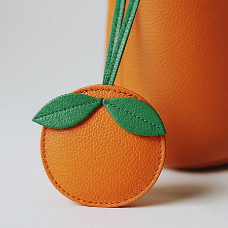 A chic orange-shaped leather bag charm with green leaf details.