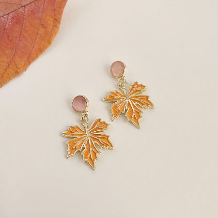 Close-up of the orange enamel maple leaf earrings with rich gold accents.