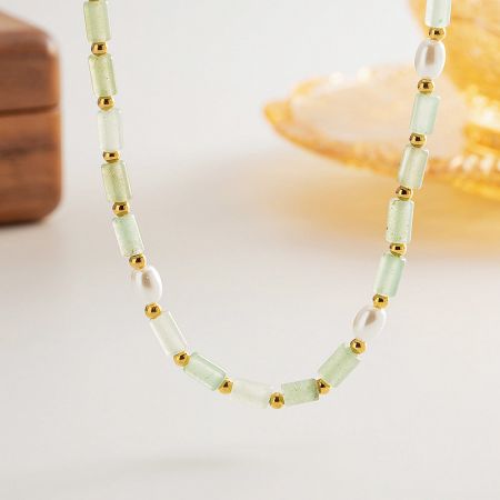 A detailed view of a boho necklace with pale green beads, gold spacers, and lustrous white pearls.