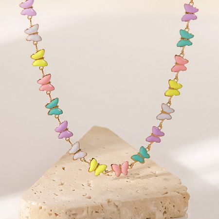 Colorful enamel butterfly necklace displayed on a beige stone.