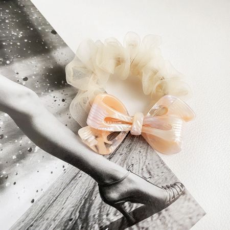 A soft peach-colored bow hair clip displayed next to a cream scrunchie.