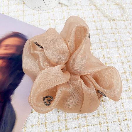 A soft peach-colored scrunchie with a bow design and heart charms.