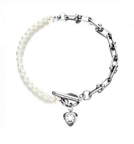 Close-up of the crystal-studded heart charm on the pearl and gold chain bracelet.