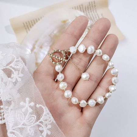 Close-up of a hand holding a 14k gold-plated pearl bracelet, highlighting the baroque pearl details.