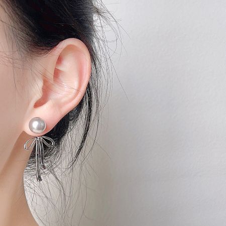 Close-up view of the pearl stud and silver bow design earring.
