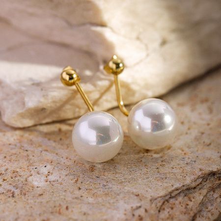 Elegant pearl stud earrings with gold posts resting on a beige stone.