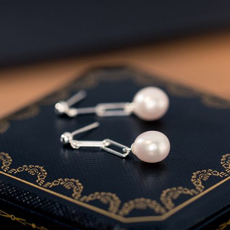 The sterling silver pearl earrings elegantly displayed on a dark surface to emphasize their shine.