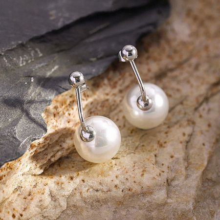 A pair of pearl stud earrings with silver-toned posts displayed on a natural rock.