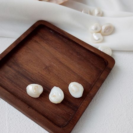 A pair of baroque pearl drop earrings presented on a rustic wooden tray.