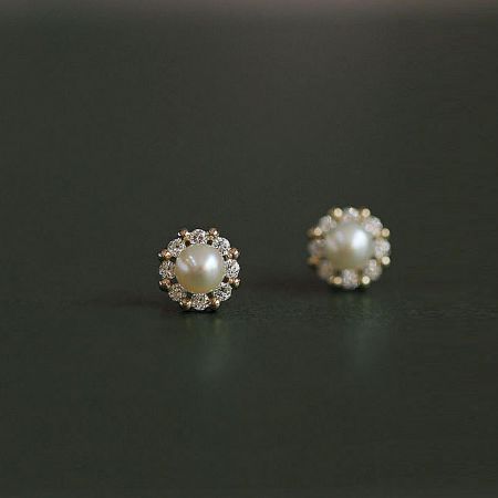 Close-up view of the pearl stud earrings with a brilliant gemstone halo.