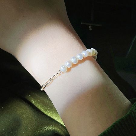 14k Gold Plated Freshwater Pearl Paper Clip Chain Bracelets (Set of 5) - A model's wrist adorned with an elegant 14k gold-plated bracelet featuring freshwater pearls and a paper clip chain design.