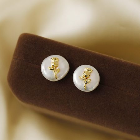 A pair of pearl-like earrings with gold rose designs shown from another angle.