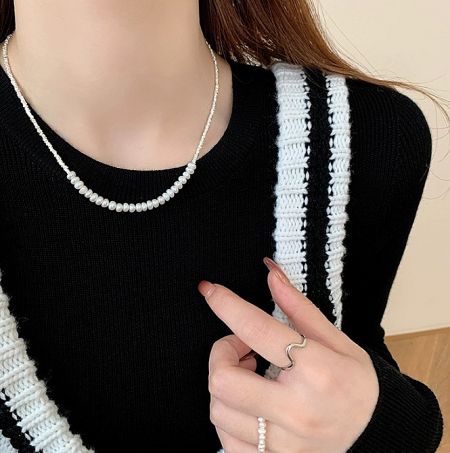 Lifestyle view of the 925 sterling silver pearl necklace worn on a black sweater, showcasing its elegant drape and style.
