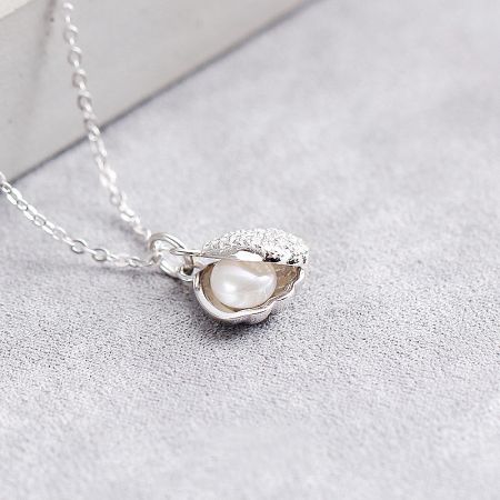 Detailed view of the sterling silver oyster shell pendant with a central pearl and sparkling crystal accents.