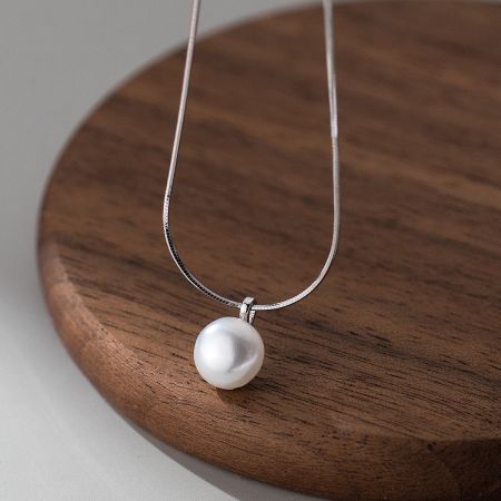 Detailed view of the pearl pendant on the choker necklace, displayed on a wooden block.