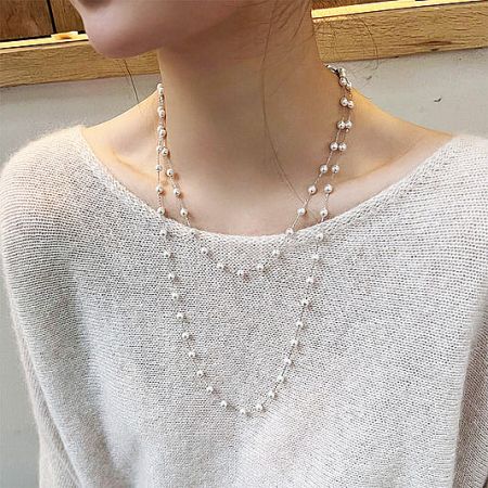 Elegant faux pearl double-layer brass necklace modeled on a white sweater.