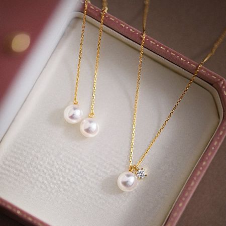 Silver and gold versions of the pearl necklace displayed in a pink jewelry box.