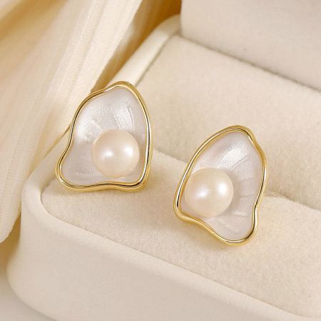 A pair of white enamel scallop pearl earrings presented in a cream-colored jewelry box.