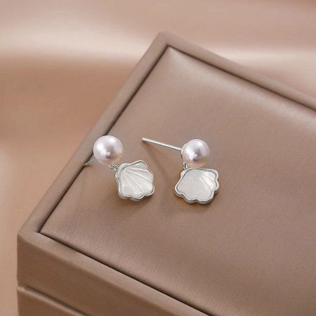 The shell and pearl drop earrings presented in a stylish tan jewelry box.